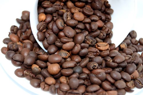Free A detailed close-up of roasted coffee beans pouring from a white cup onto a surface. Stock Photo
