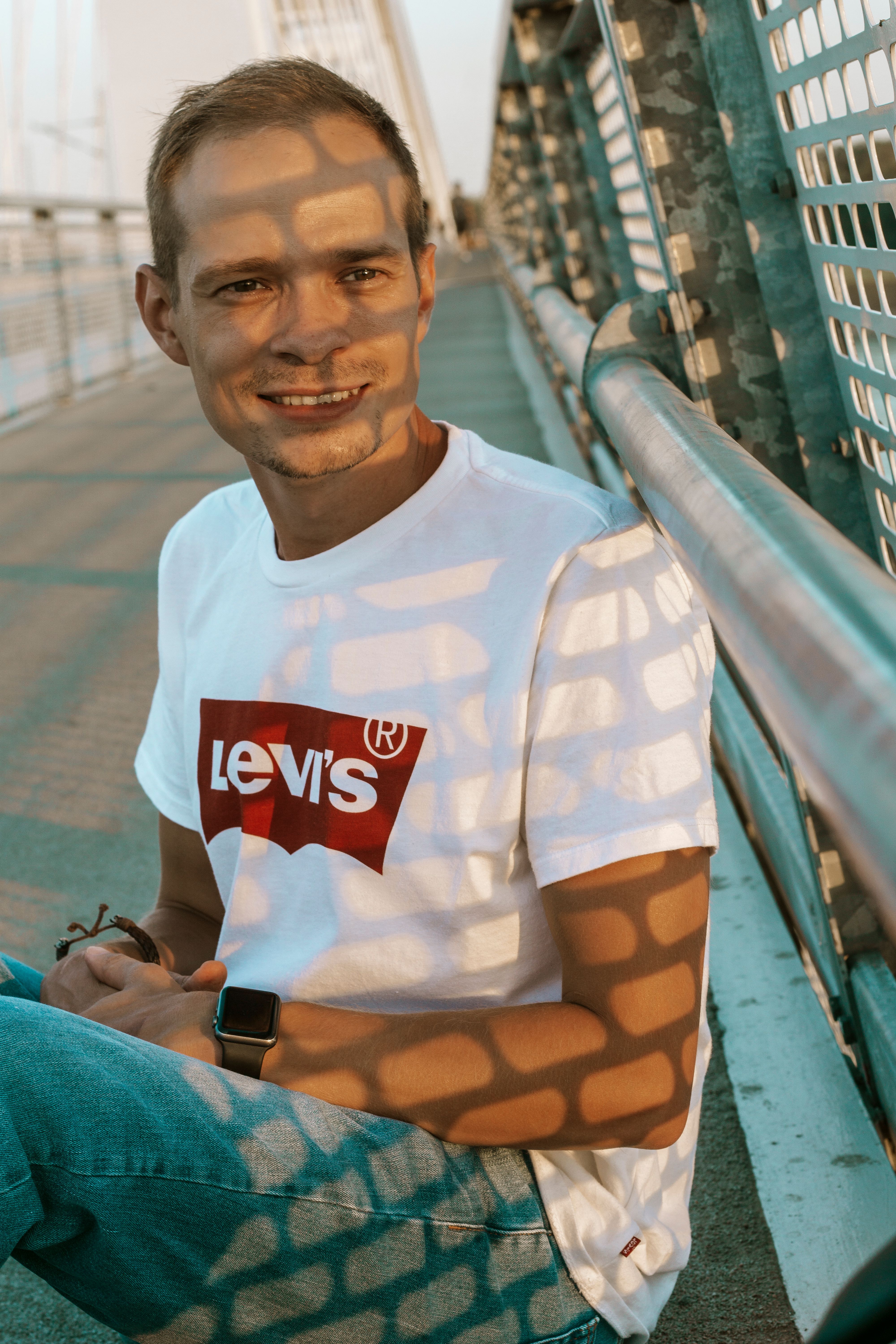 Young smiling male in stylish t shirt looking away on city bridge in sunlight