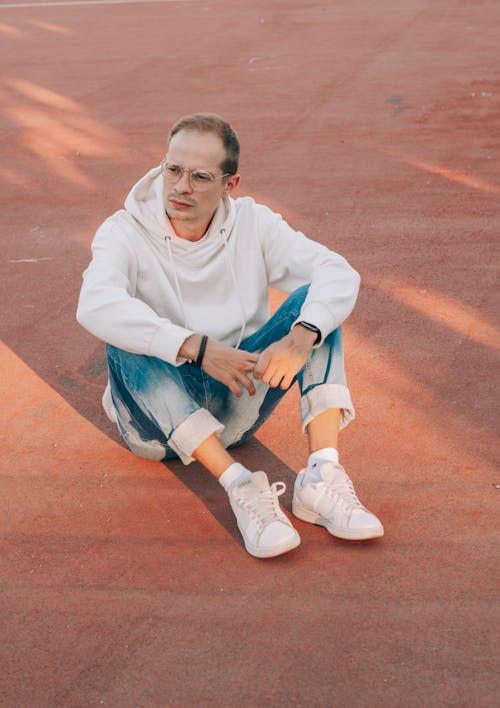 Stylish man in hoodie resting on sports ground