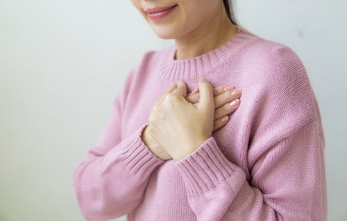 Free Content anonymous female wearing warm pink sweater standing on white background with crossed hands on chest in daylight in room Stock Photo