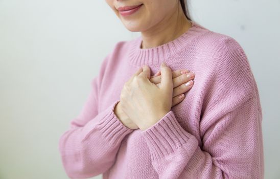 Content anonymous female wearing warm pink sweater standing on white background with crossed hands on chest in daylight in room