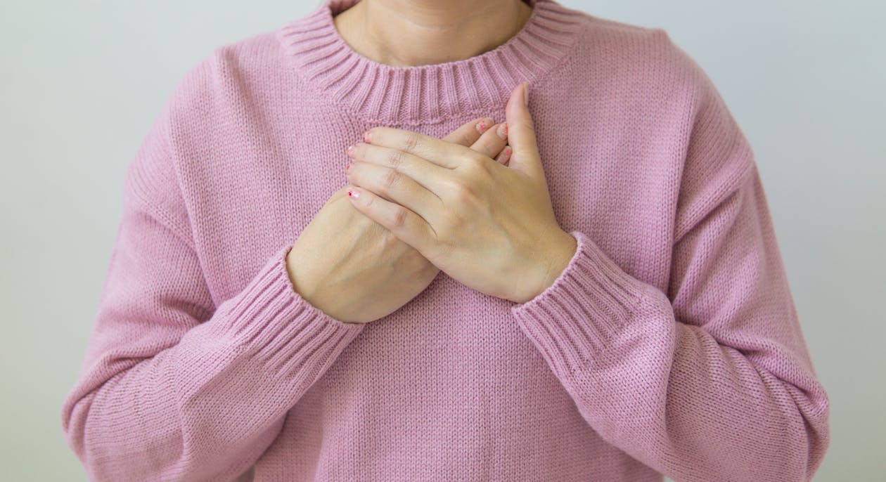 Free Unrecognizable female wearing pink sweater standing on white background with crossed hands on chest in light room in daytime inside Stock Photo