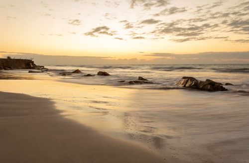 Free Golden hour at a tranquil beach in Alagoas, Brazil with waves and rocks in view. Stock Photo