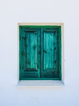 Retro green wooden shuttered window on a white exterior wall. Simple and classic.