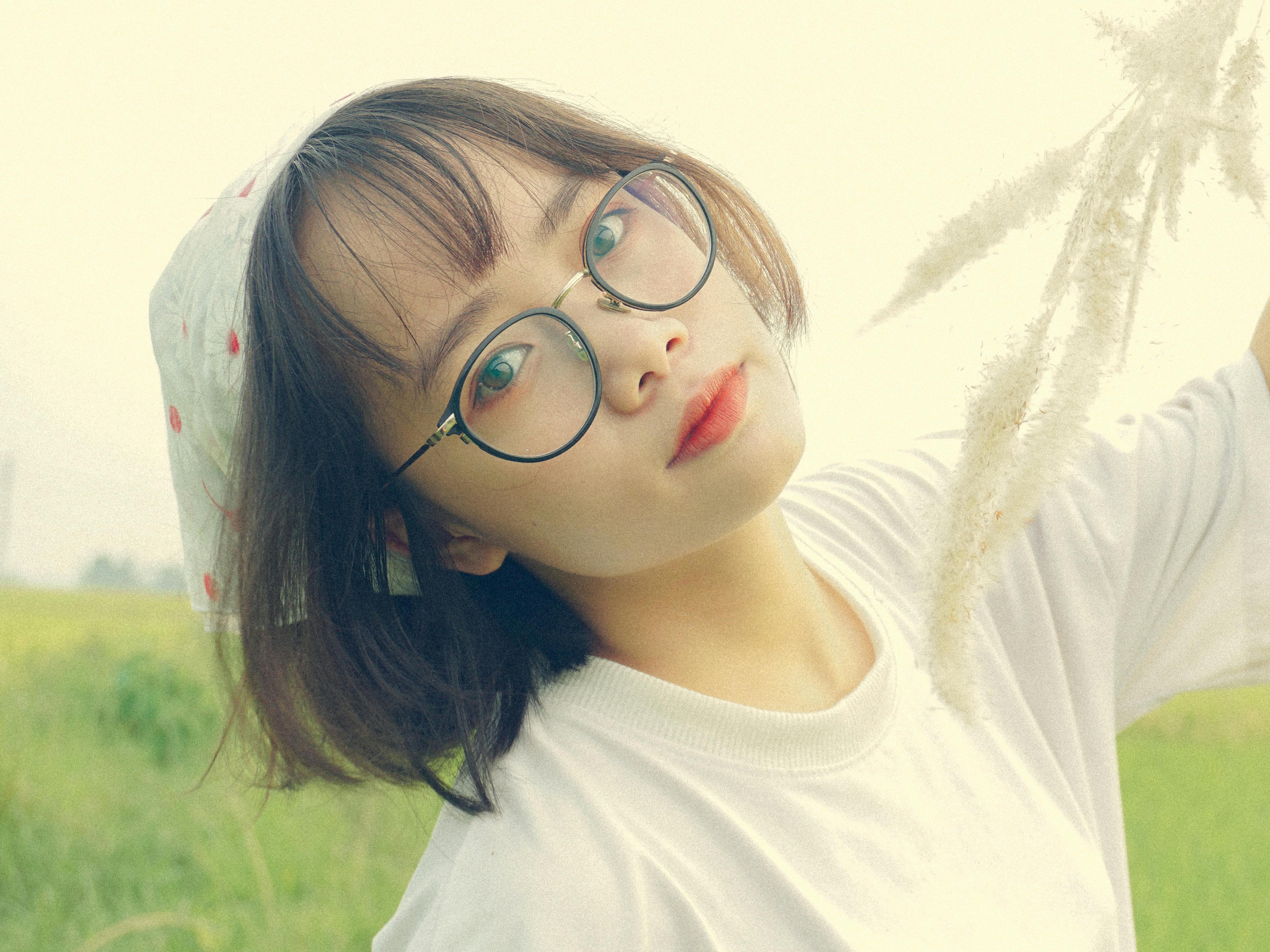 Portrait of an Asian woman with glasses in a serene field setting.