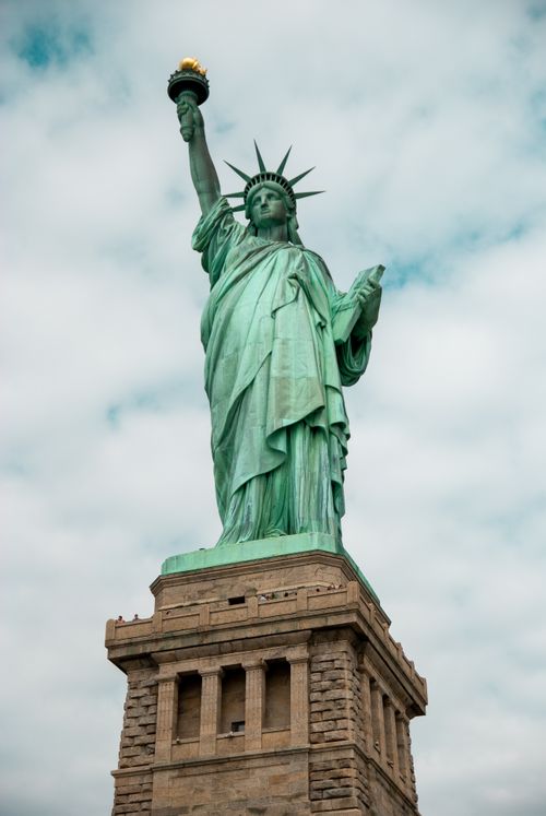 Free The iconic Statue of Liberty standing tall against a backdrop of partly cloudy skies in New York City. Stock Photo
