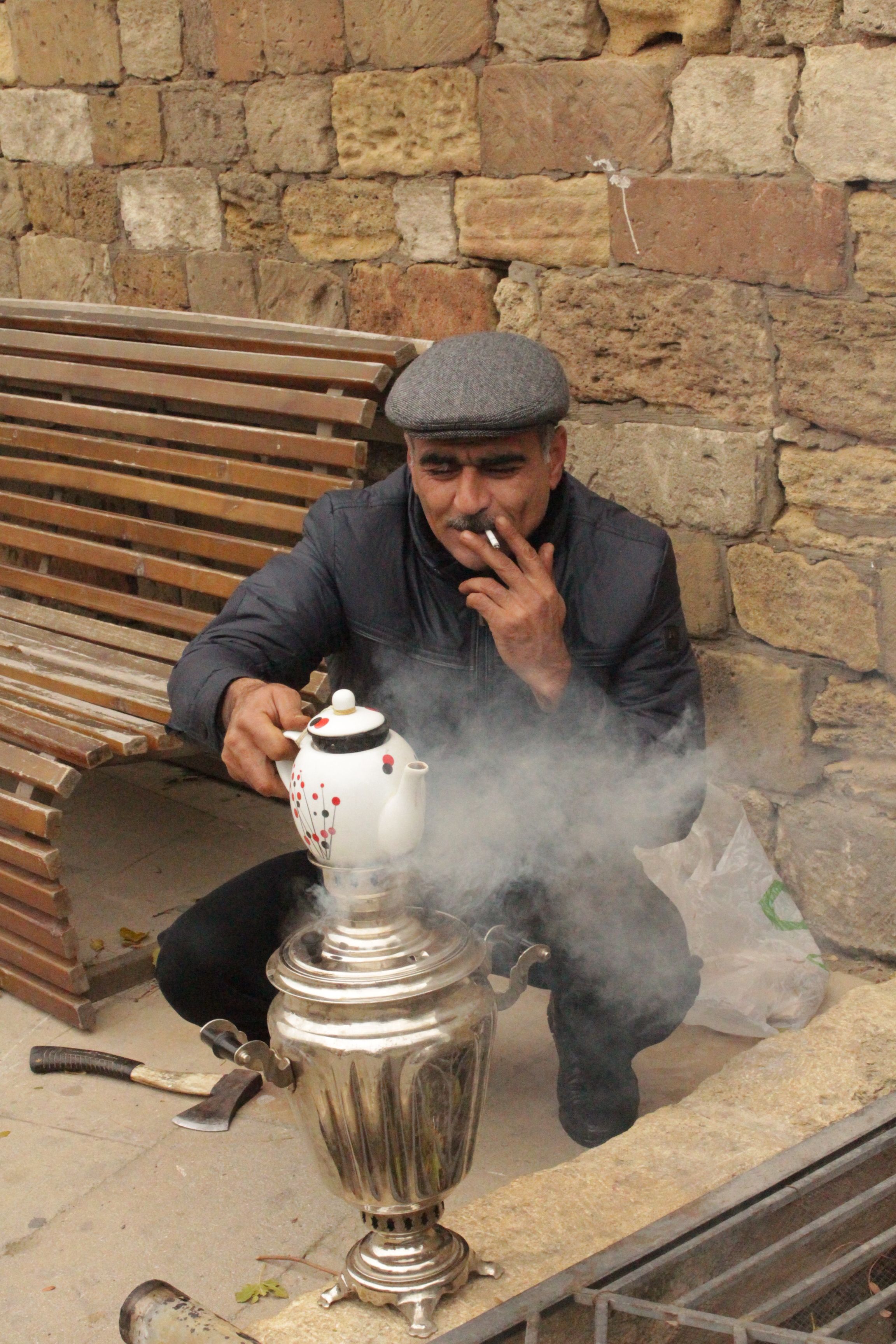 A man in Baku smoking and brewing tea with a samovar in an outdoor setting.