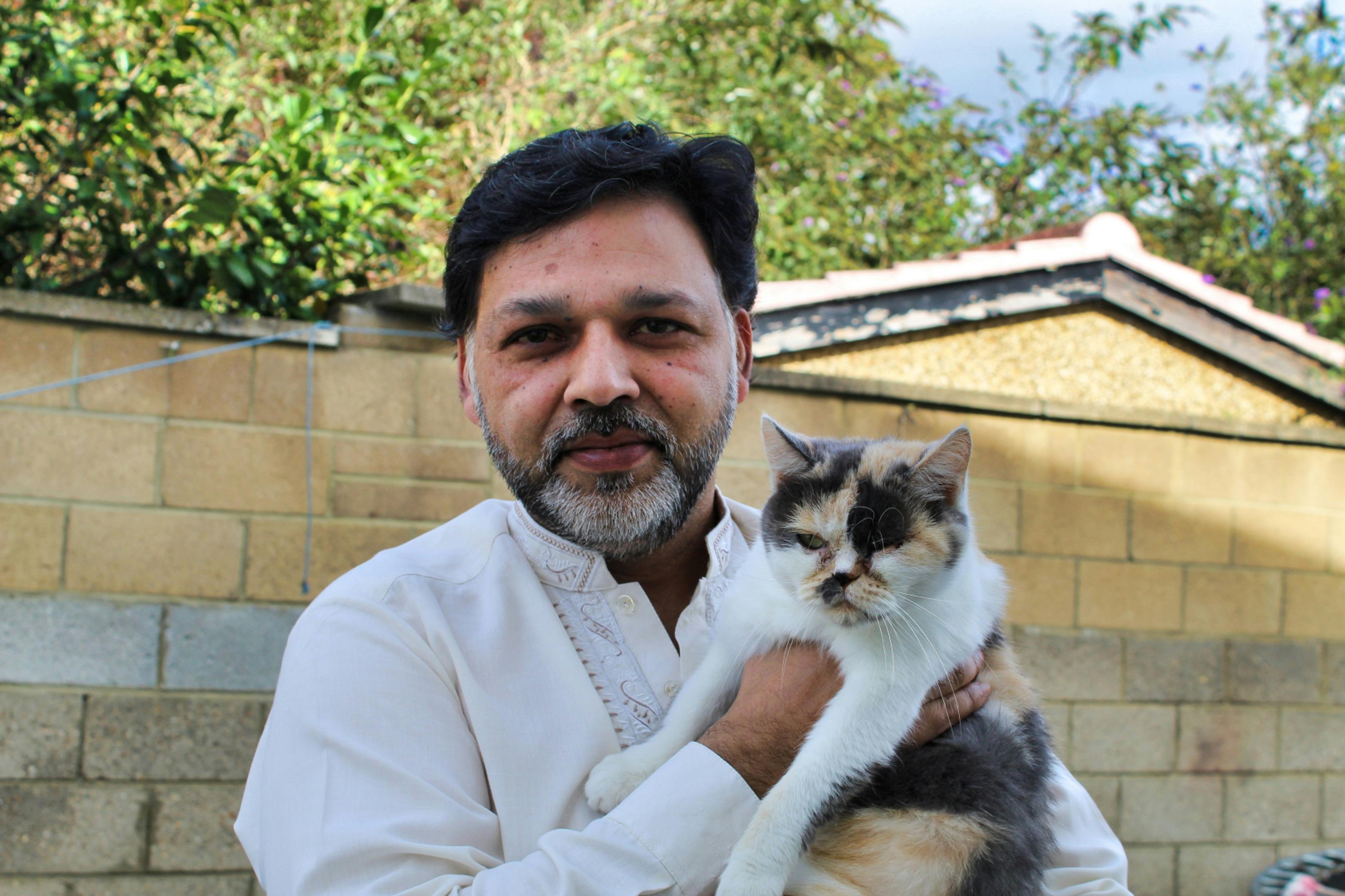 A bearded man smiling while holding a fluffy cat outside.