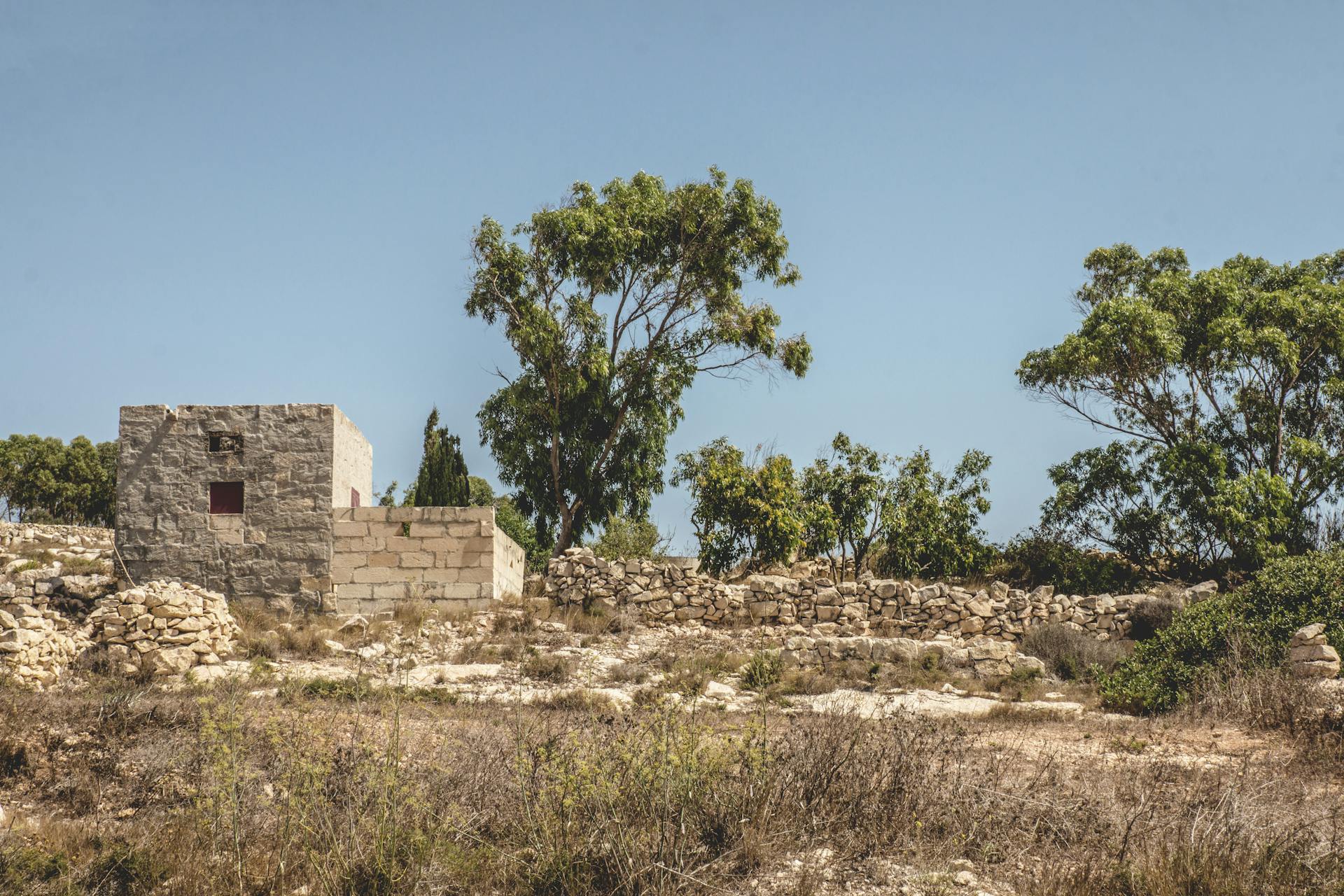 Explore the tranquil historic ruins in Mgarr, Malta with stone structures and lush trees.