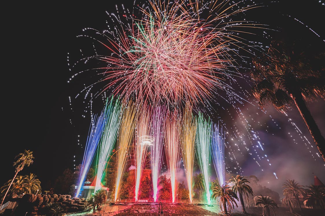 Long exposure of vibrant sparkling fireworks and bright multi colored Roman candles over palms and pavement at night