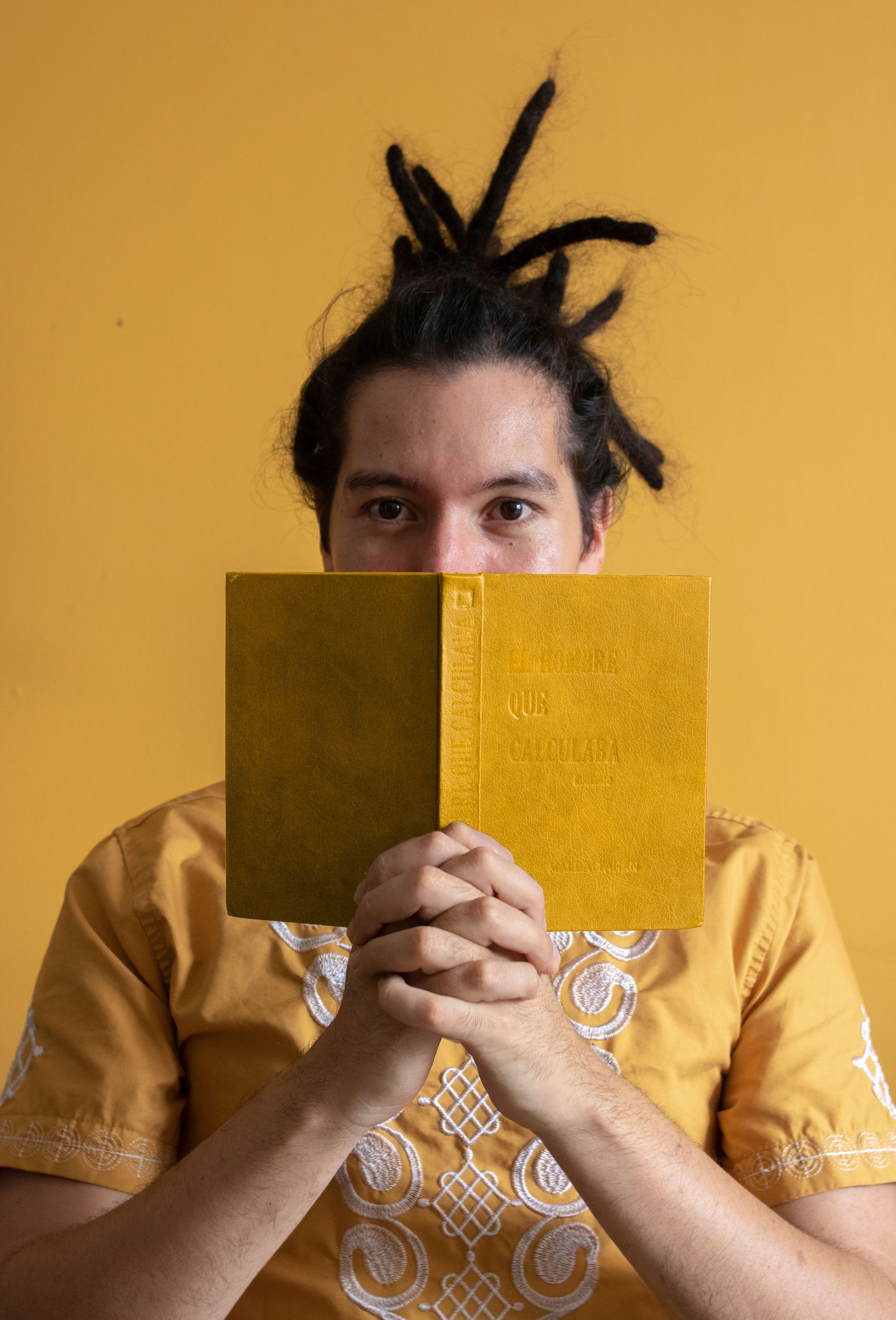 Man wearing embroidered shirt holds a yellow book in front of a matching background.