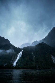 Dramatic waterfall flows down a foggy mountain, surrounded by lush greenery in a serene setting.