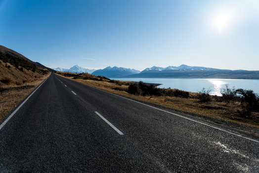 A picturesque road with a view of mountains and a lake under a clear sky.
