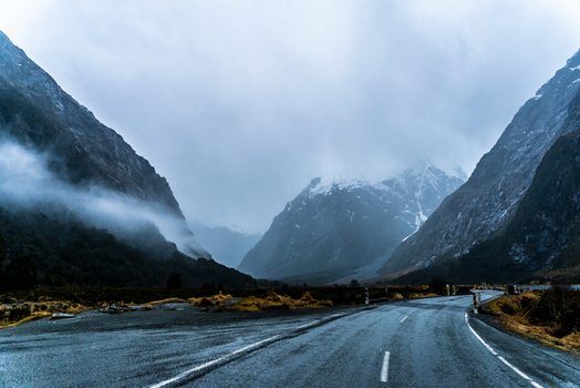 Foggy mountain road with snow-capped peaks under cloudy winter sky, perfect for travel and nature themes.