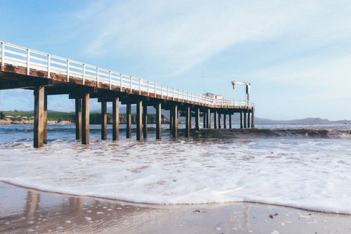 Free A peaceful wooden pier extends over the ocean with gentle waves and a clear sky. Stock Photo