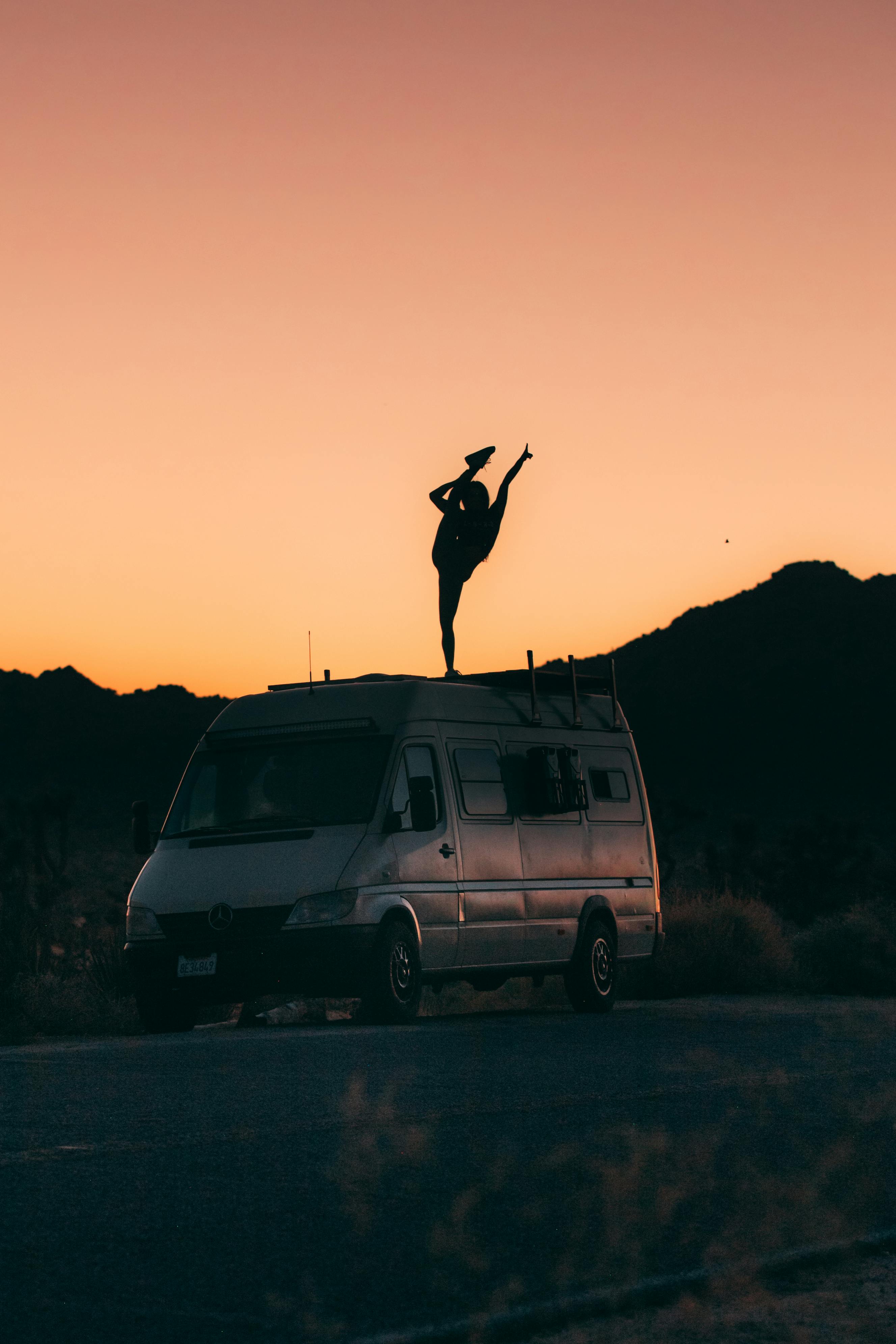 A silhouette of a person standing on a van against a stunning sunset in a California desert.