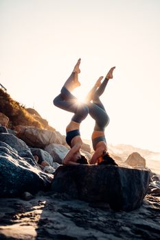 Two women performing acro yoga on rocks during sunset in Malibu, showcasing balance and flexibility.
