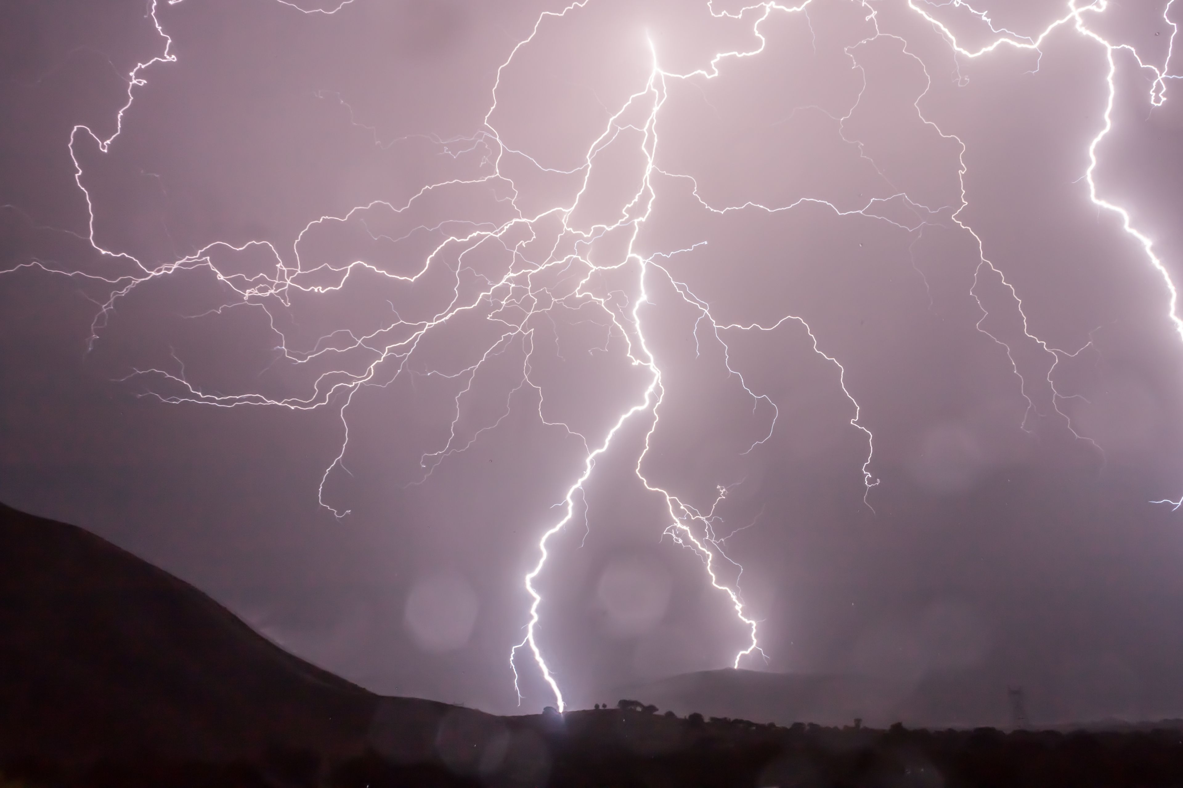 Captivating lightning bolts illuminate the night sky over dark hills in a dramatic weather display.