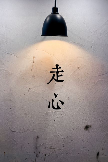 Close-up of illuminated Chinese characters on a textured wall under a stylish lamp.