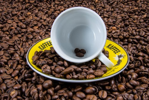 White Ceramic Cup on Yellow Plate With Coffee Beans