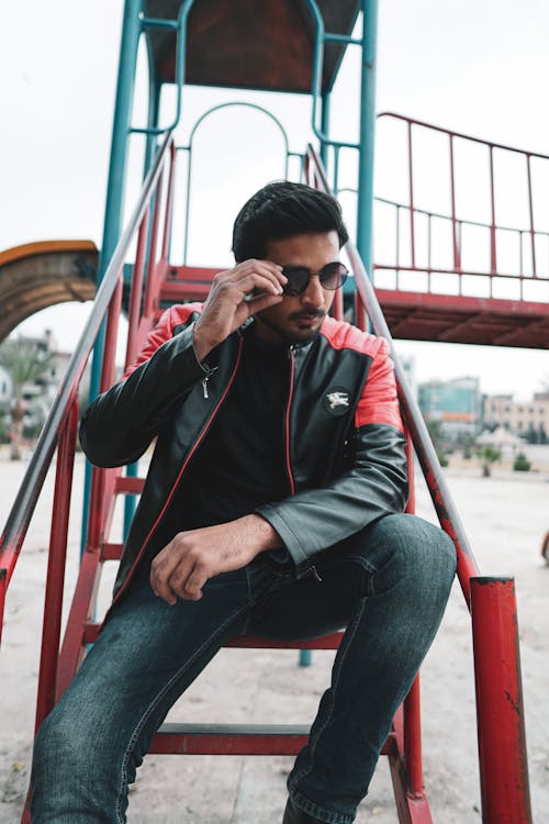 A Man in Leather Jacket Sitting on the Park while Holding His Sunglasses