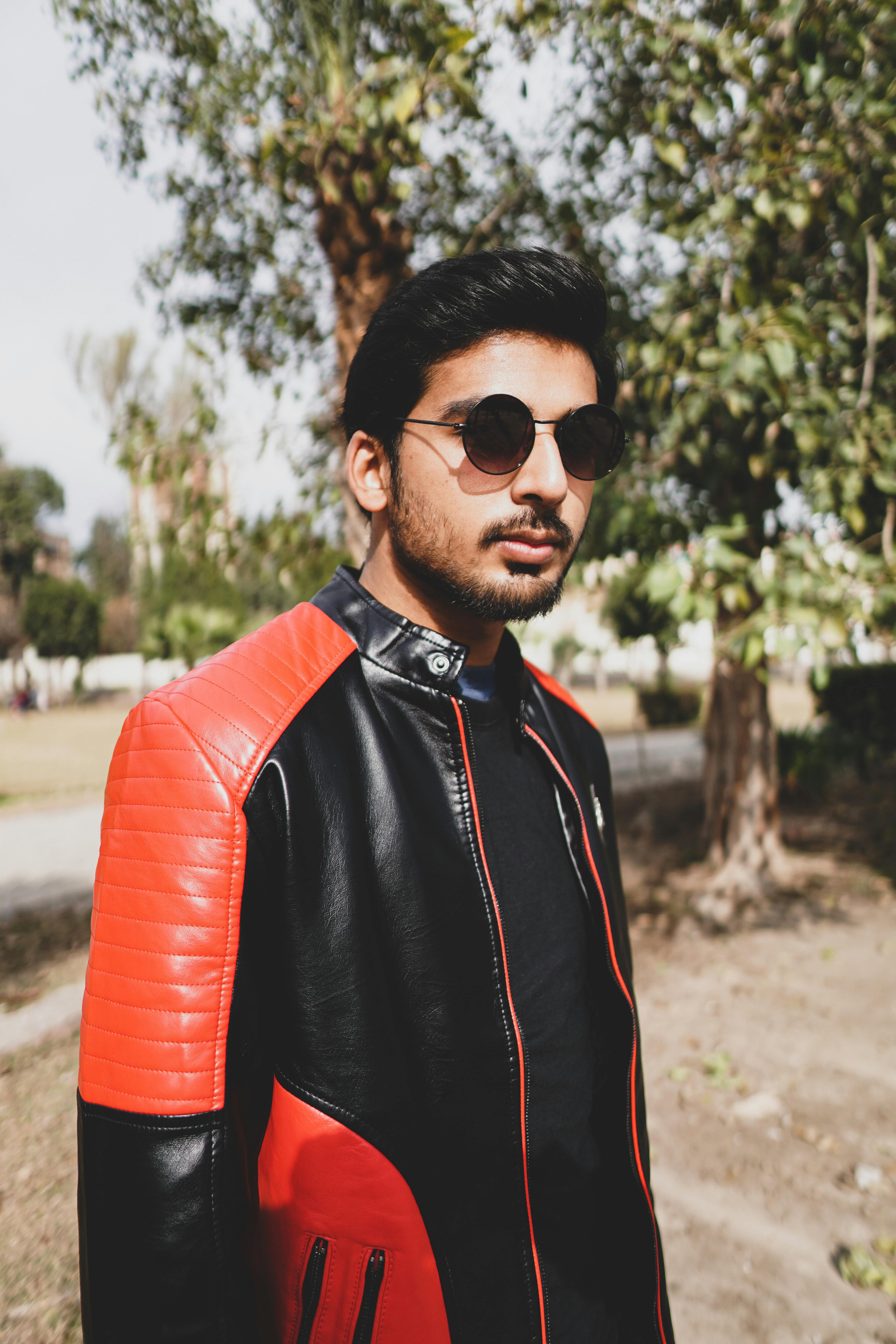 Stylish man in sunglasses and leather jacket in a sunny outdoor setting.