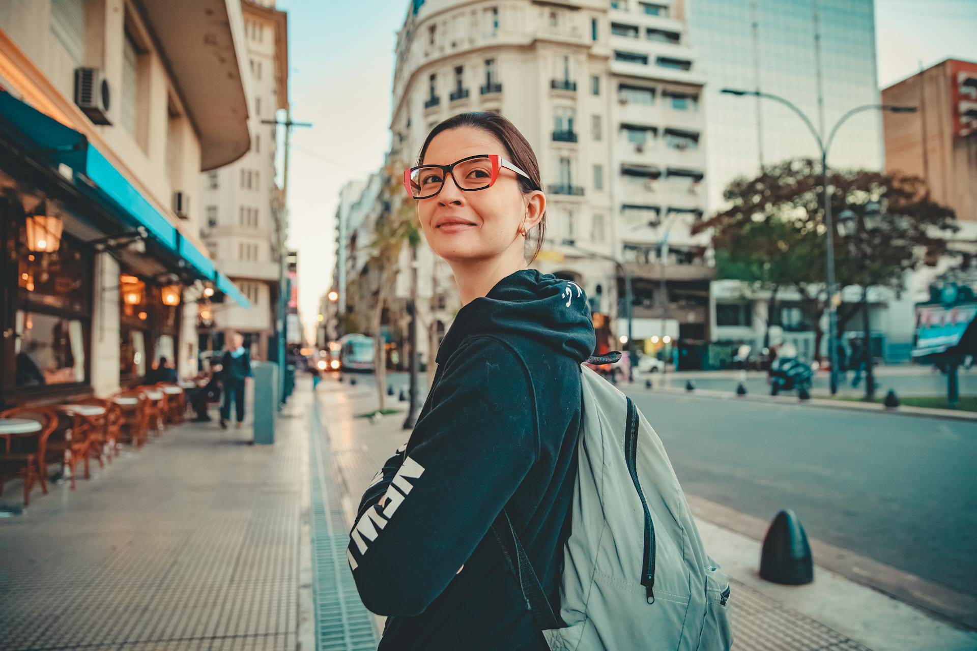 Woman in hoodie and glasses smiles while walking on a city street in San Nicolás, Argentina.