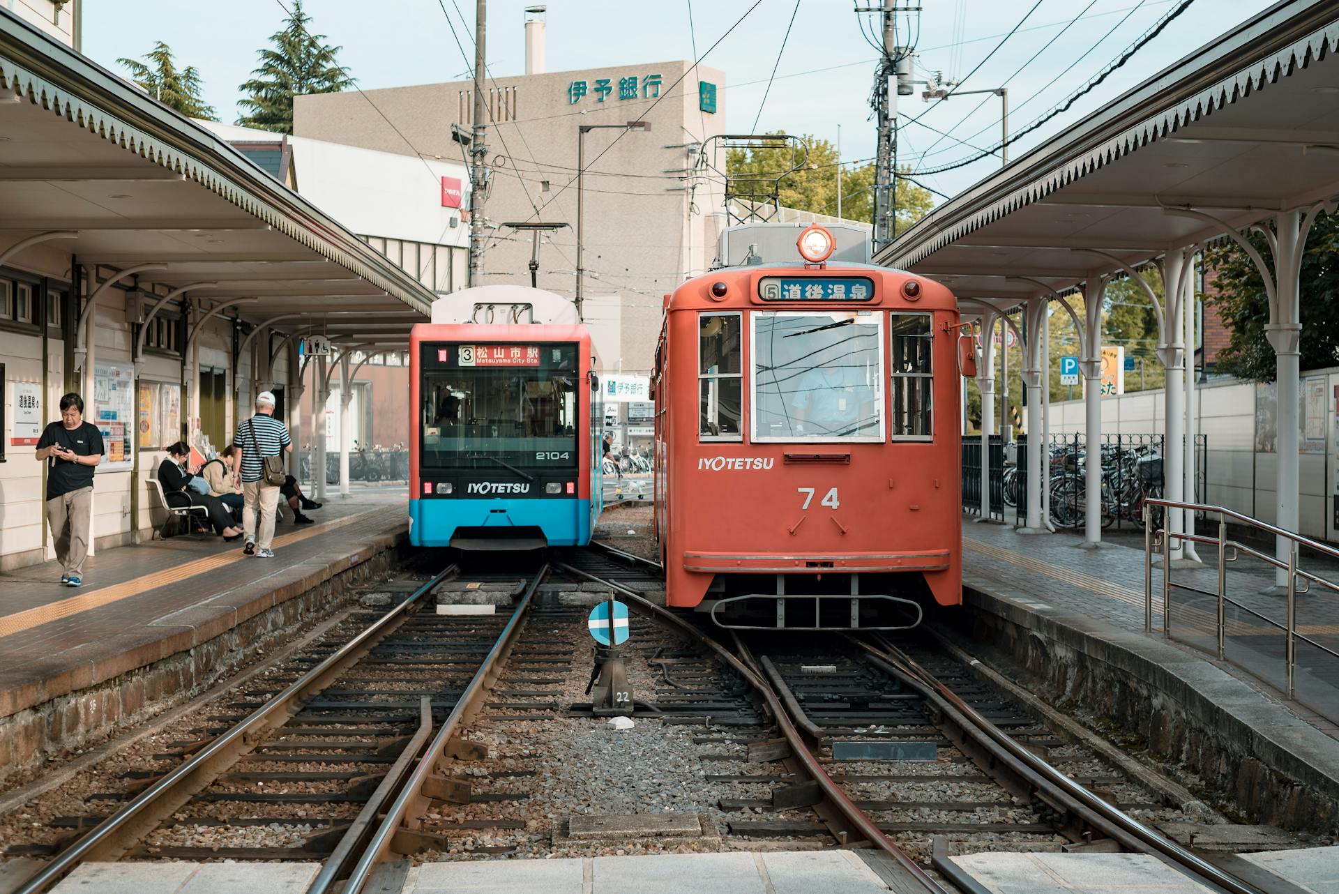 Scenic view of a tram station in Japan with two colorful trains and passengers.