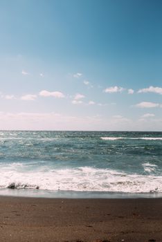 A serene view of ocean waves gently hitting a sandy beach under a clear blue sky.