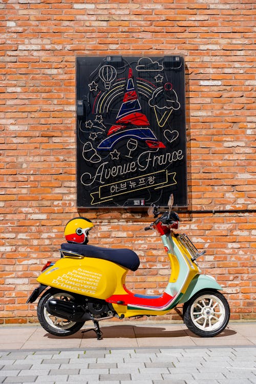 Red and Yellow Motor Scooter Parked Beside Brown Brick Wall