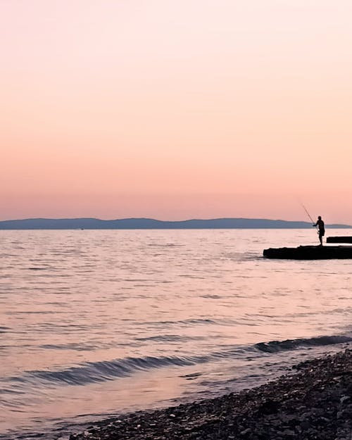 A Silhouette of a Person Fishing on the Sea