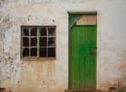 Aged building exterior with a vibrant green door and broken window, capturing a rustic charm.