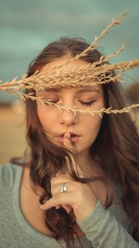 一位闭着眼睛、手指轻触嘴唇的女子，在麦田环绕的户外环境中，留下了一幅宁静的肖像