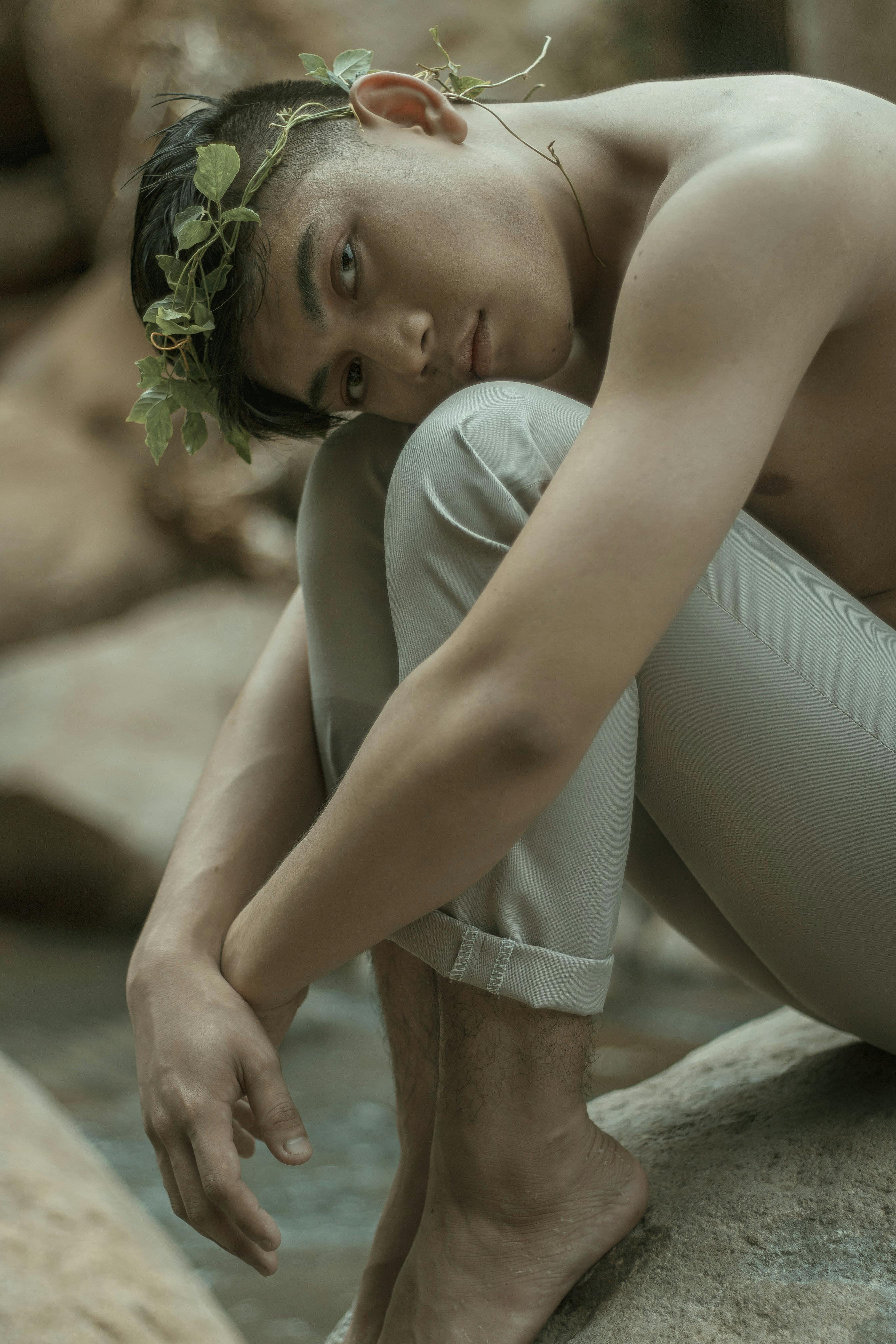 光着膀子的年轻人坐在河边沉思，绿树成荫的花环装饰着四周，散发着宁静的气息