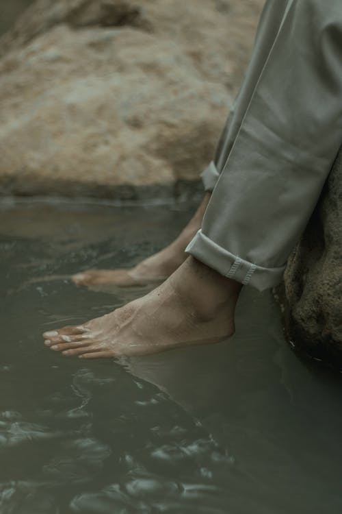 Unrecognizable person resting on river shore with feet in water