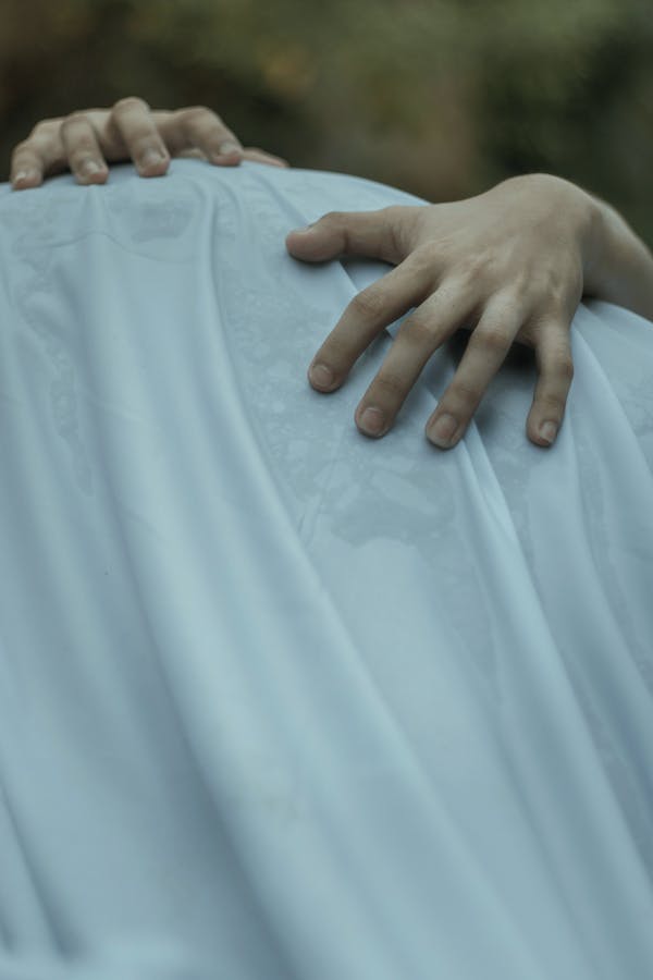 Crop unrecognizable person touching wet sheet with fingers on blurred background of greenery