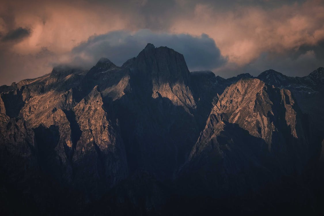 Splendid landscape of rough mountain cliffs under cloudy sky in sunlight in evening