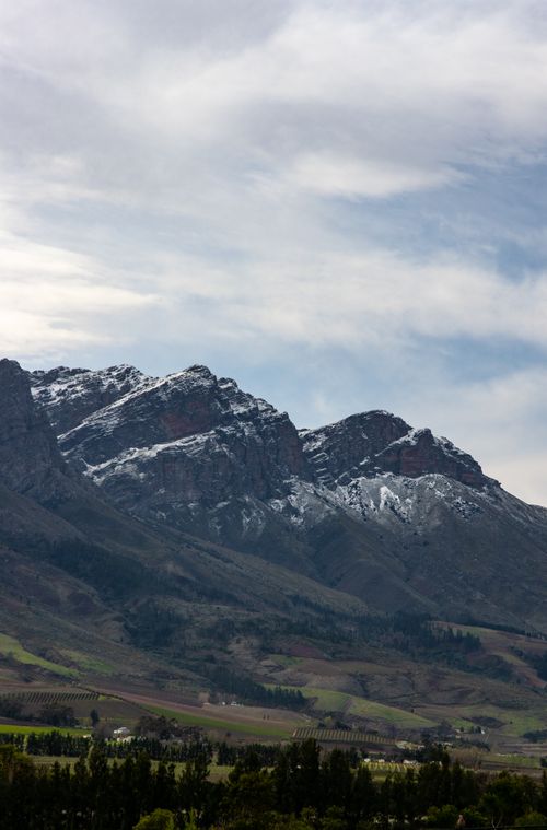 Free Breathtaking view of snow-capped Tulbagh mountains in South Africa, surrounded by lush landscape under a cloudy sky. Stock Photo