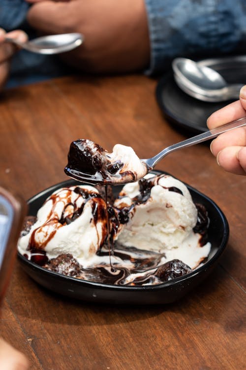 Close-up of Person Holding Vanilla Ice Cream with Chocolate Sauce on a Spoon 