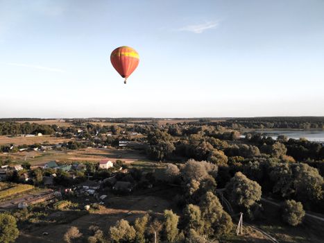 A colorful hot air balloon floats over lush rural landscape during daytime.
