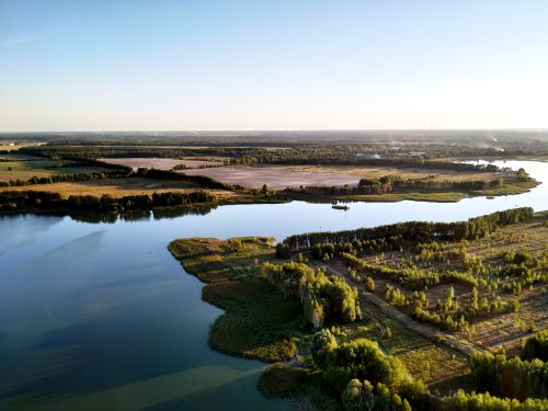 Free A stunning aerial view of a tranquil lake surrounded by lush forests under a clear blue sky during sunset. Stock Photo