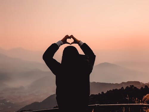 Free Woman Making Heart Shape with Hills in Background Stock Photo
