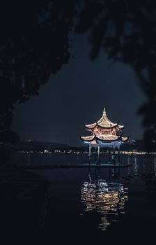 一座灯火通明的中国传统宝塔矗立在水面上，倒映在宁静的夜色中