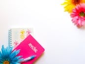 白色背景上，笔记本、笔和鲜花色彩明亮而丰富