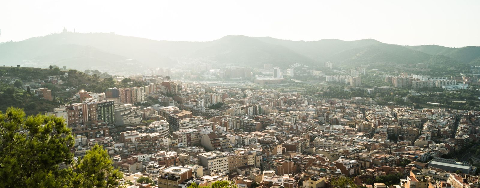 Aerial view capturing Barcelona's urban landscape surrounded by mountains and hills during daylight.