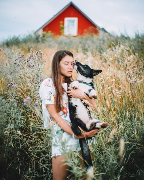 grátis Mulher Magra Segurando Cachorro Em Um Prado Por Casa Sob Um Céu Cinza Foto profissional