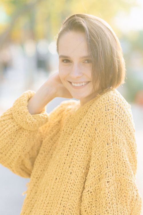 Free A woman in a yellow knitted sweater smiles brightly outdoors. Capturing warmth and joy. Stock Photo