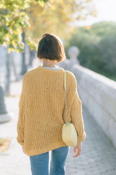 阳光明媚的日子里，一个女人穿着舒适的针织毛衣和牛仔布裤子在公园散步