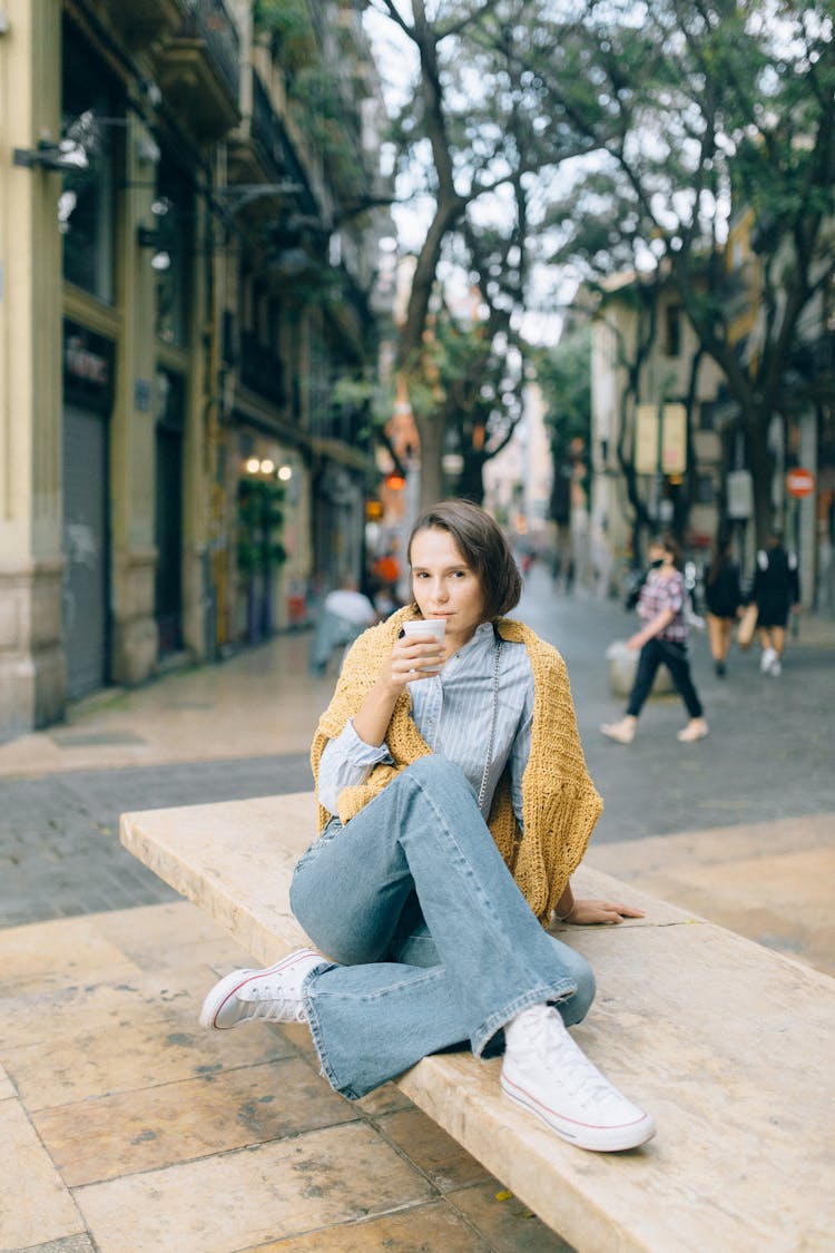 A Young Woman Holding A Styrofoam Cup While Sitting On A Bench