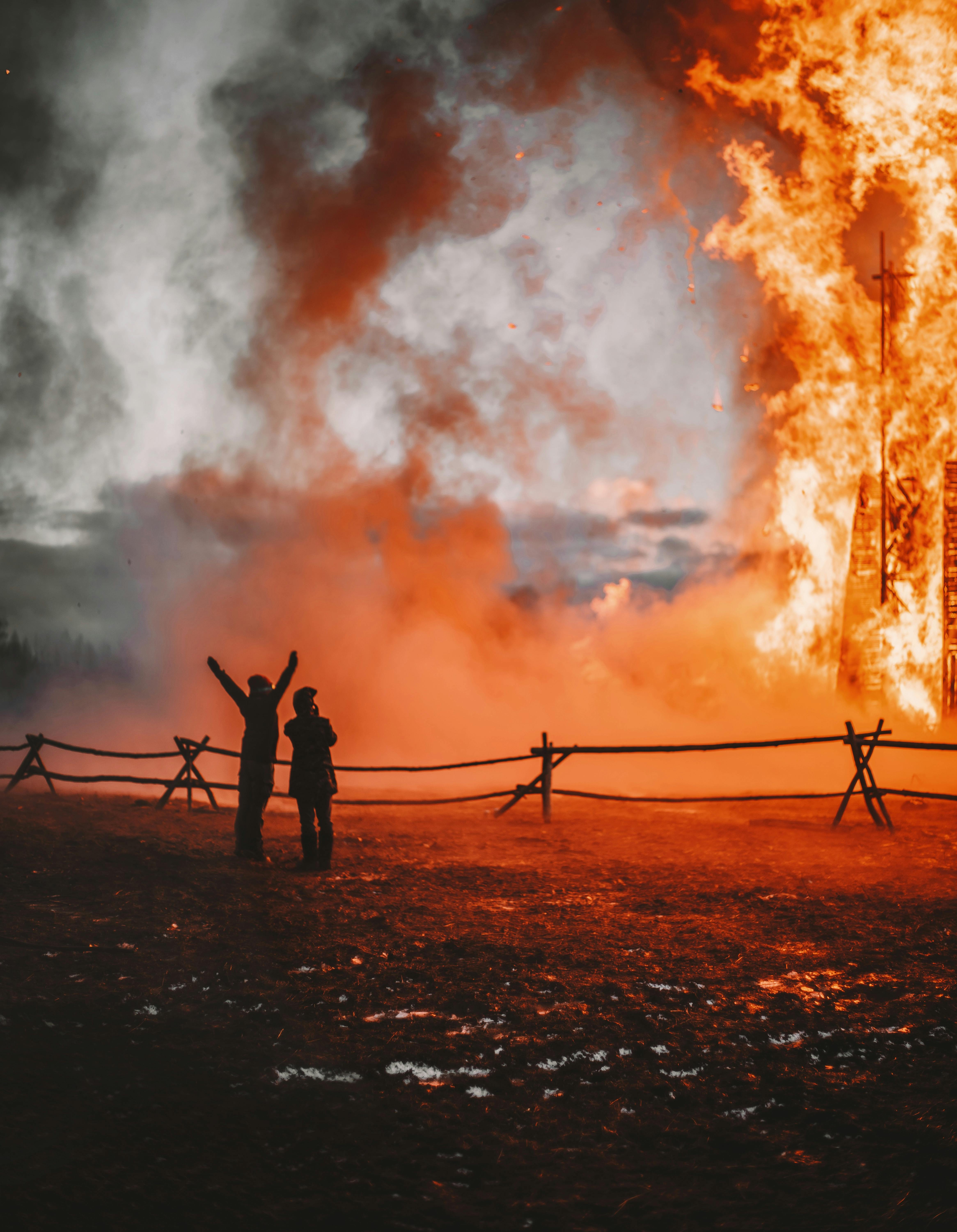 silhouetted of people standing and looking at a large fire